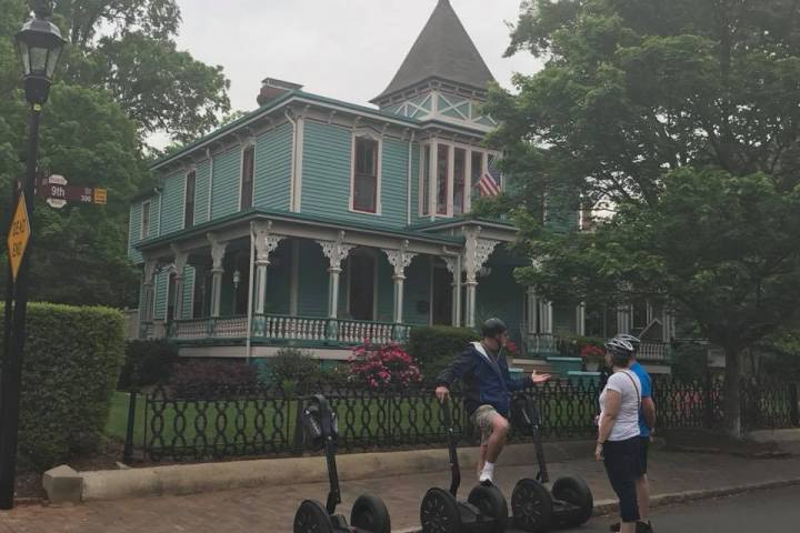 A guide explaining the history behind a wooden old style house to two guests on Segways