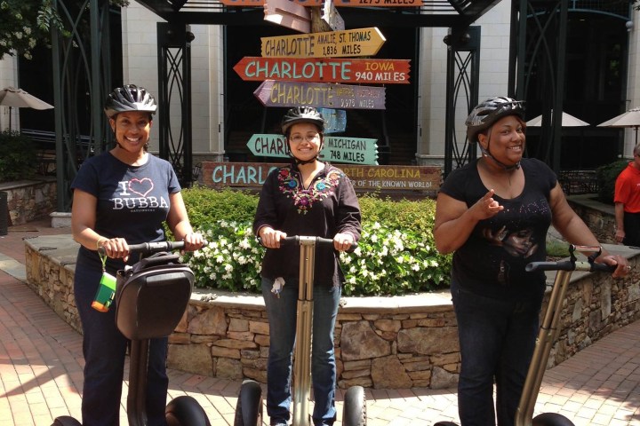Three women smiling on Segways in front of a directions sign