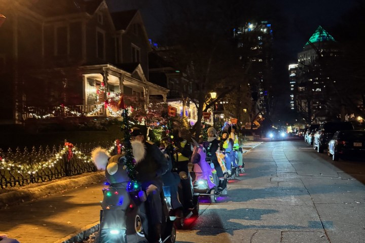 People on decorated scooters in a nighttime parade on a city street.